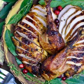 Overhead shot of Garlic and Herb Roast Turkey , carved, sliced and on an wooden platter with fresh bay leaves and loose cranberries.