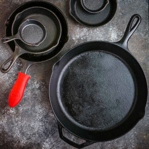 Different size cast iron skillets arranged on a table, one with a red handle protector.