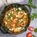 Overhead shot of roasted eggplant pasta in a cast iron dutch oven garnished with fresh basil, with basil and a sliced tomato alongside.