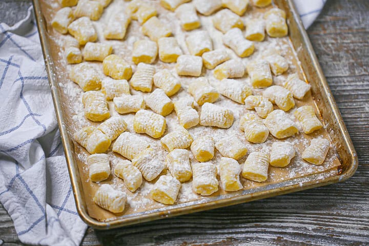 Close up of homemade potato gnocchi floured and uncooked on a sheet pan.