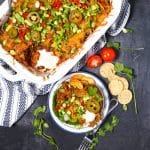 Beef Taco Casserole with a scoop taken out and placed on a serving plate with chips and tomatoes scattered around.