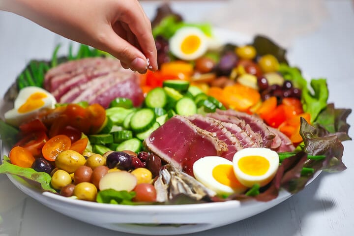 Sprinkling salt onto a Seared Tuna Nicoise Salad.