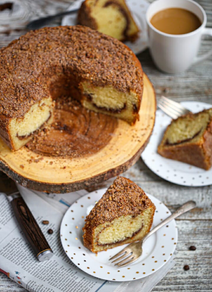 Slices of sour cream coffee cake on plates next to cake on a wooden cake plate.